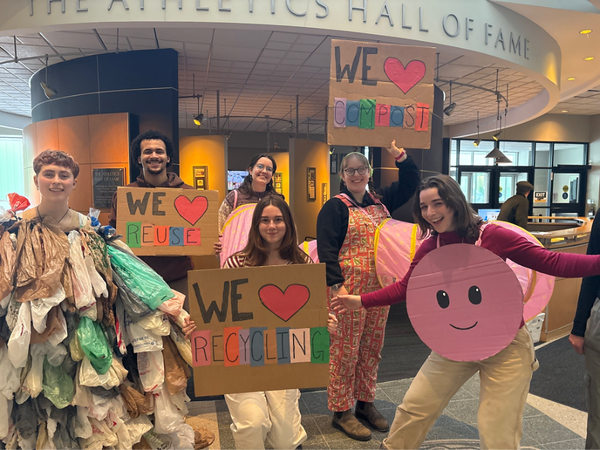 Group of students promoting sustainability with signs encouraging recycling, reuse, and composting.