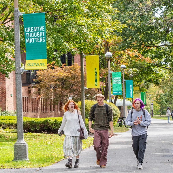 Three students walk together on Թ’s campus, passing banners that read ‘Creative Thought Matters.