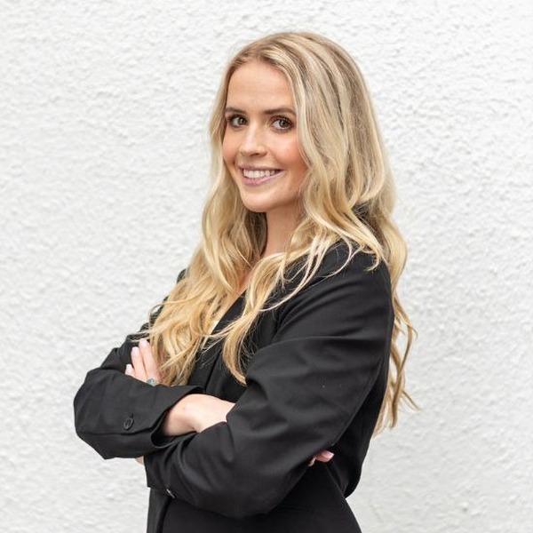 Paige Karl headshot: She wears all black and stands in front of a white wall