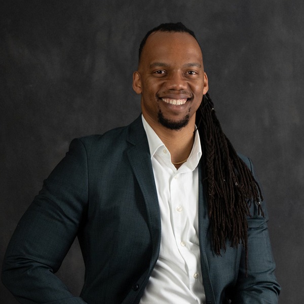 Portrait of Skidmore alum Theko Lekena ’16 smiling, wearing a dark blazer and white shirt against a neutral studio background