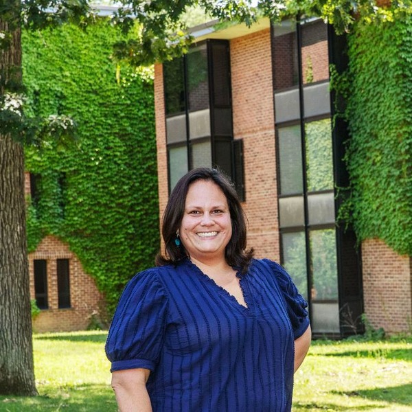 Smiling woman in a navy blouse stands in front of an ivy-covered brick building
