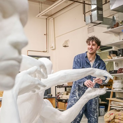 A student artist in a sculpture studio works on a large white figurative piece