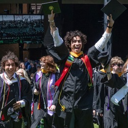 Graduates celebrate joyfully as they walk across the commencement stage, holding up their diplomas in caps and gowns.