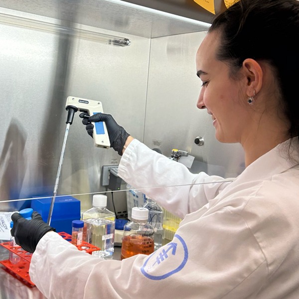 Scientist in a lab coat using a pipette inside a biosafety cabinet.