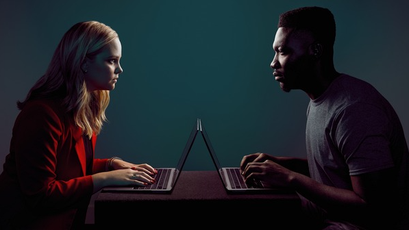 Two people on computers staring at each other menacingly